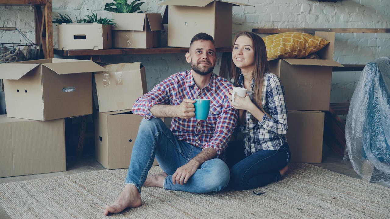 Happy couple sitting among moving boxes, enjoying coffee in their new home.